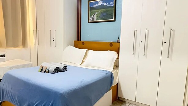 Ein Schlafzimmer mit Bett, einem Fenster mit Vorhängen, einem Bild an der Wand und einem Kleiderschrank.