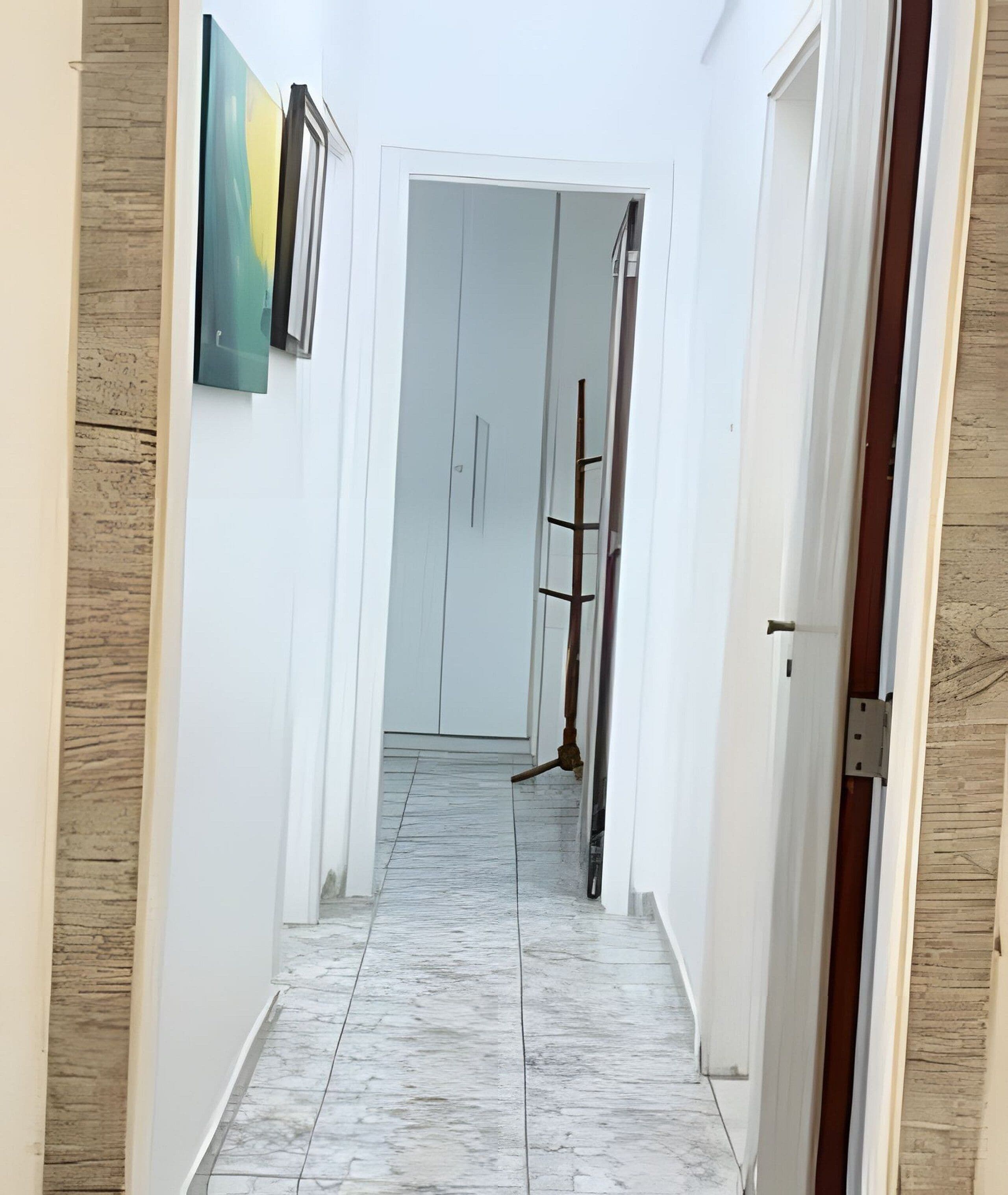 A hallway with white walls, a marble floor, and a door at the end.