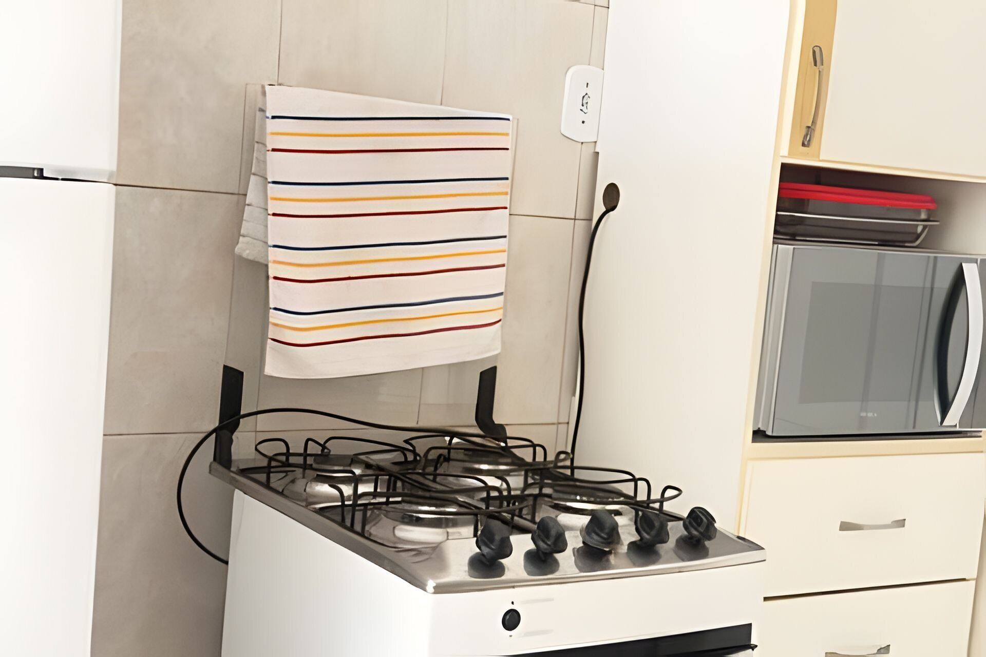 A kitchen with a gas stove, a striped towel hanging on the wall, and a microwave.