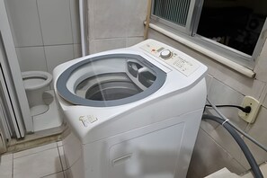 En frontbetjent vaskemaskine med kontrolpanel, et vindue og et synligt strømstik.