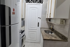 Uma cozinha compacta com armários brancos, pia de aço inoxidável e micro-ondas.