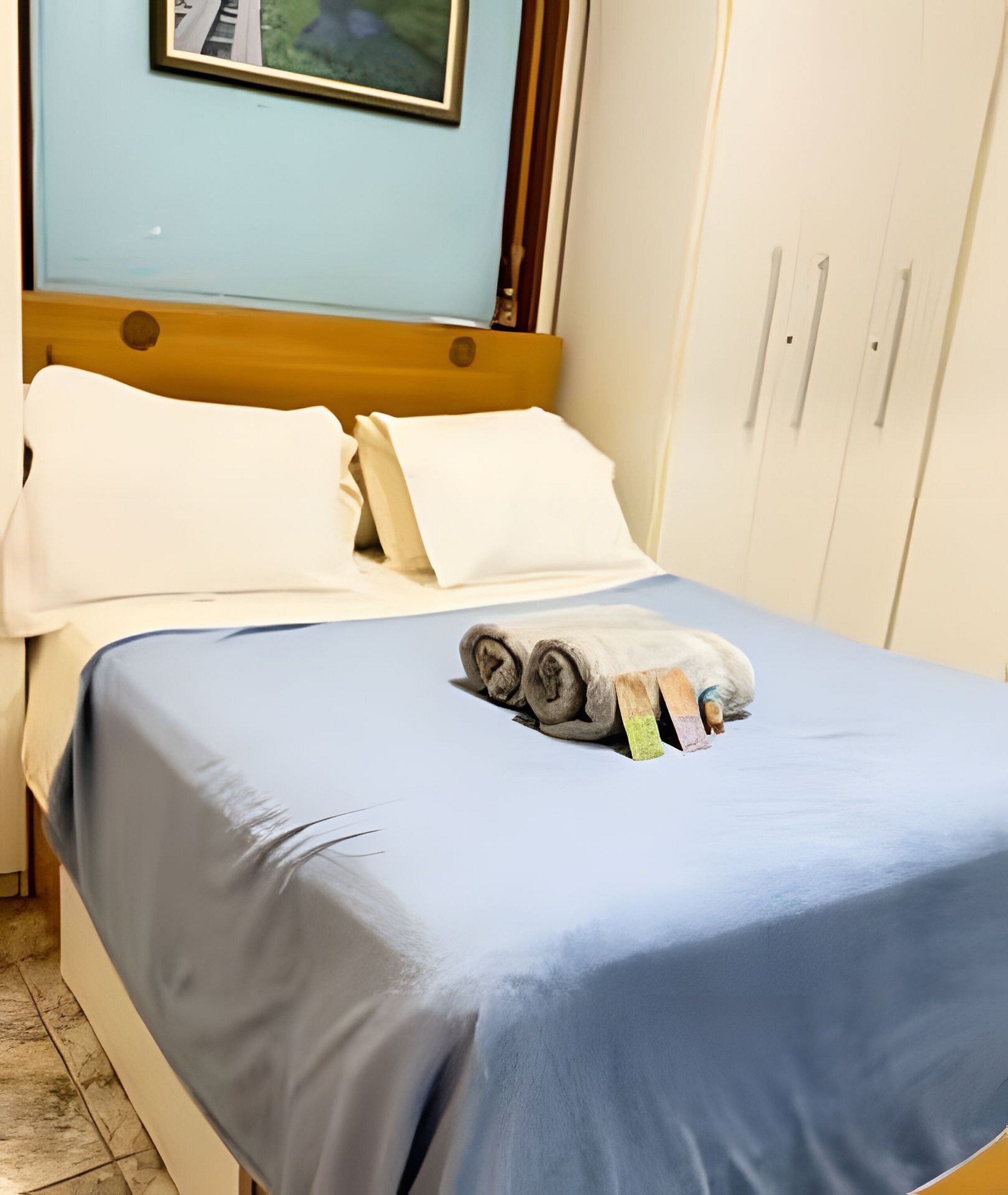 Un letto con una coperta blu, cuscini bianchi e un asciugamano arrotolato.