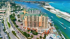 A multi-story hotel with a green roof, located near a marina with boats and a beach. - 3BR Harborfront Condo - Pool, Hot Tub, Bay Shuttle (Destin)