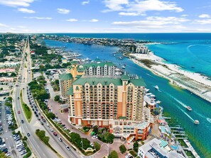 Ein mehrstöckiges Hotel mit Gründach in der Nähe eines Yachthafens mit Booten und einem Strand.