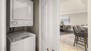 A modern kitchen with a built-in washer and dryer, a dining area with a table and chairs, and a large window. - 3BR Harborfront Condo - Pool, Hot Tub, Bay Shuttle (Destin)