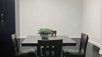 Un coin repas comprenant une table rectangulaire, quatre chaises, une plante en pot et un luminaire suspendu au plafond.