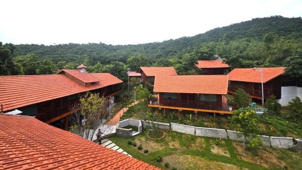 Un barrio residencial con varios edificios de techos rojos, rodeado de vegetación y colinas.
