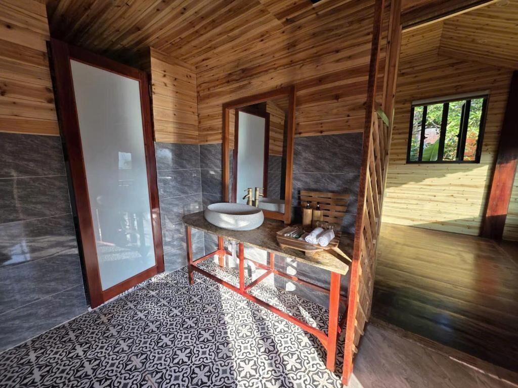 A bathroom with a wooden ceiling, a large mirror, a sink, and a patterned floor.