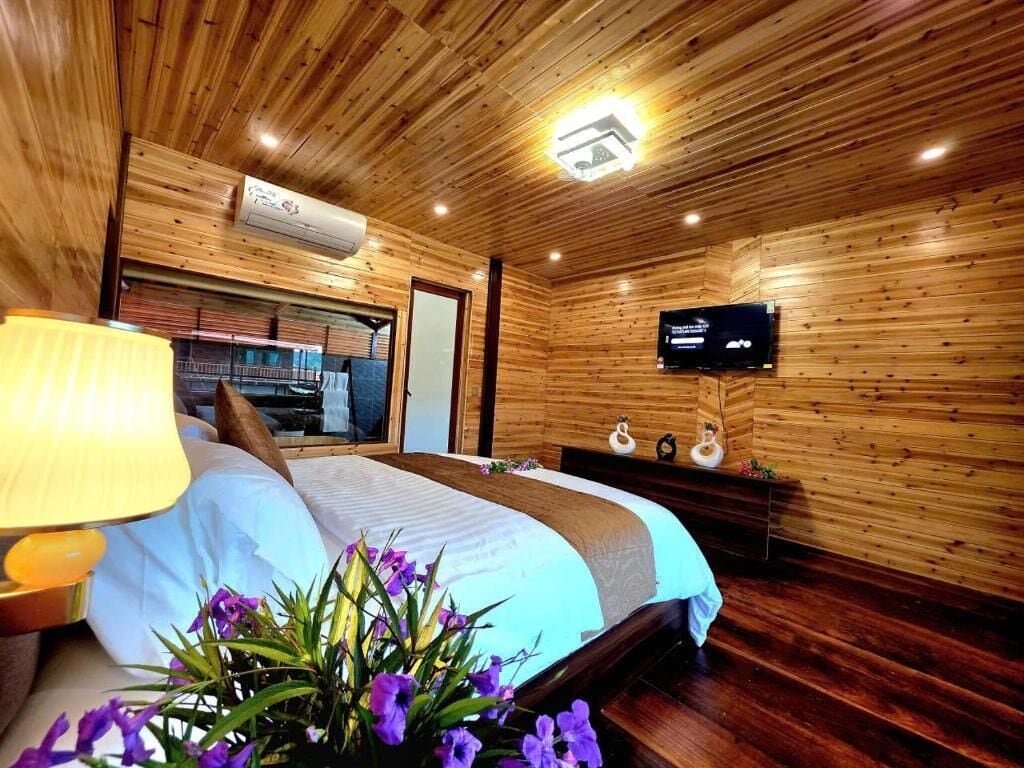 A wooden-paneled room with a bed, a television mounted on the wall, and a window.