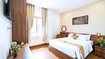A hotel room with a large bed, bedside tables, a TV mounted on the wall, and a window with curtains.
