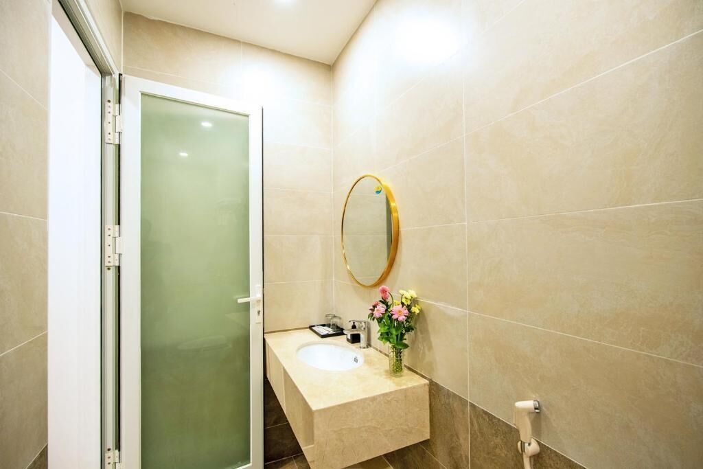 A bathroom with a glass shower door, a sink with a mirror, and a vase with flowers.