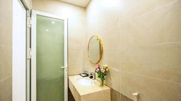 A bathroom with a glass shower door, a sink with a mirror, and a vase with flowers.