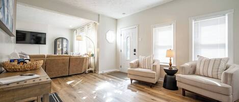 A spacious living area with a wooden floor, a sofa, a coffee table, and a television mounted on the wall.