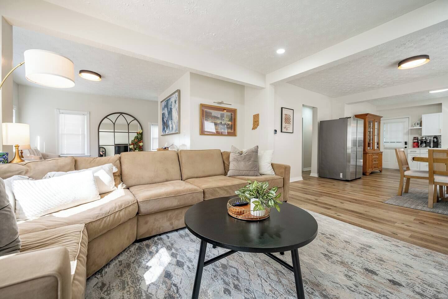 Ein modernes Wohnzimmer mit einem beigen Sofa, einem Couchtisch mit Pflanze und einer Küche im Hintergrund.