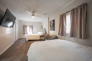 A hotel room with two beds, a ceiling fan, a flat-screen TV, and a painting on the wall. - 10 Min to Lucas Oil~Walk to Mass Ave~Hot Tub (Indianapolis)