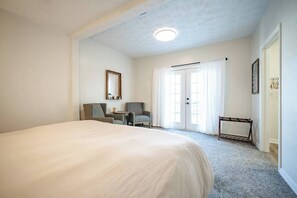 A hotel room with a large bed, two chairs, a small table, a mirror, and a door with curtains. - 10 Min to Lucas Oil~Walk to Mass Ave~Hot Tub (Indianapolis)