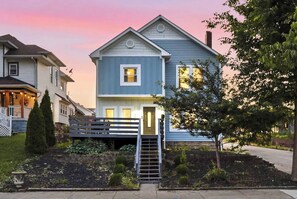A two-story residential house with a front porch, a small staircase leading to the entrance, and a well-maintained garden. - 10 Min to Lucas Oil~Walk to Mass Ave~Hot Tub (Indianapolis)