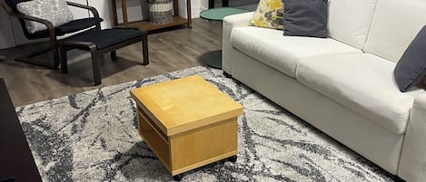 Een woonkamer met een witte bank, een houten salontafel, een zwart-wit tapijt met een patroon, een ronde spiegel en een klein bijzettafeltje.