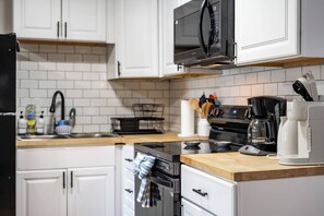 A modern kitchen with white cabinets, a black microwave, a coffee maker, and a stove. - Quaint Downtown Indy~Walk to Mass Ave~Nearby Park (Indianapolis)