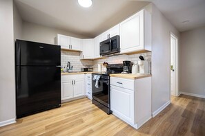 A compact kitchen with white cabinetry, a black refrigerator, a microwave, and a stove. - Quaint Downtown Indy~Walk to Mass Ave~Nearby Park (Indianapolis)