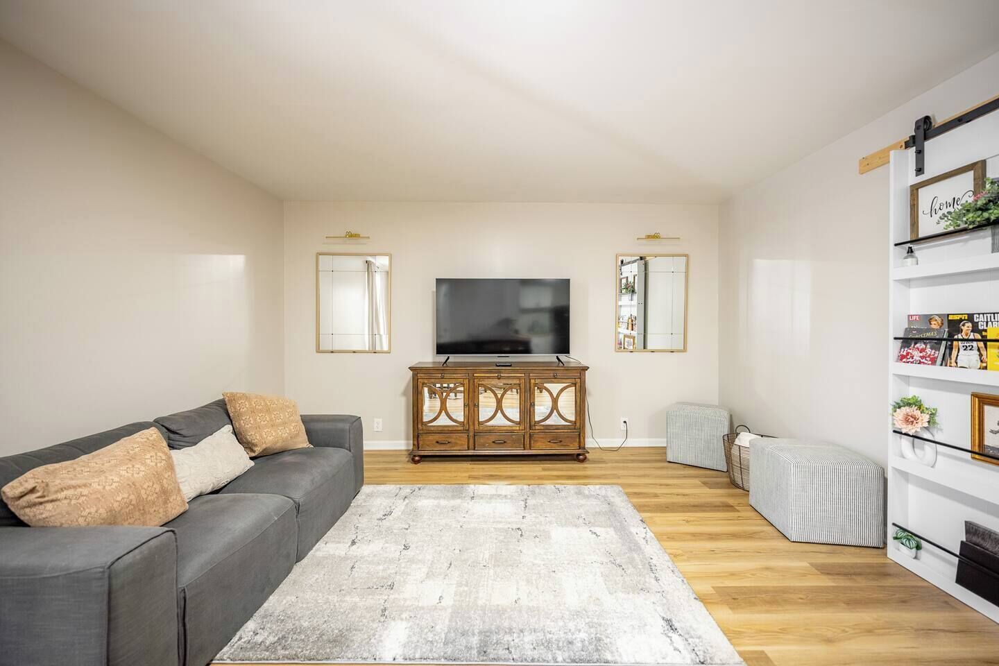 A living room with a grey sofa, wooden cabinet, flat-screen TV, and a bookshelf.