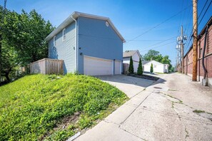 A residential street with a single-story house, a garage, and a small front yard with grass and a wooden fence. - Quaint Downtown Indy~Walk to Mass Ave~Nearby Park (Indianapolis)