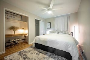 Ein Schlafzimmer mit einem Bett, einem Schreibtisch, einem Deckenventilator und einem an der Wand befestigten Regal mit einem Zitat.