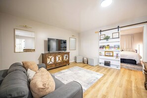 A modern living room with a grey sofa, wooden cabinet, flat-screen TV, and a bookshelf. - Quaint Downtown Indy~Walk to Mass Ave~Nearby Park (Indianapolis)