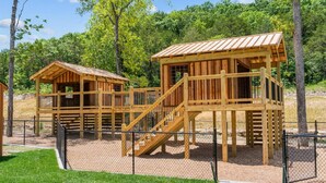 A wooden play structure with a staircase and a separate playhouse. - The Lazy Beaver Lodge - Hot Tub (Hollister)