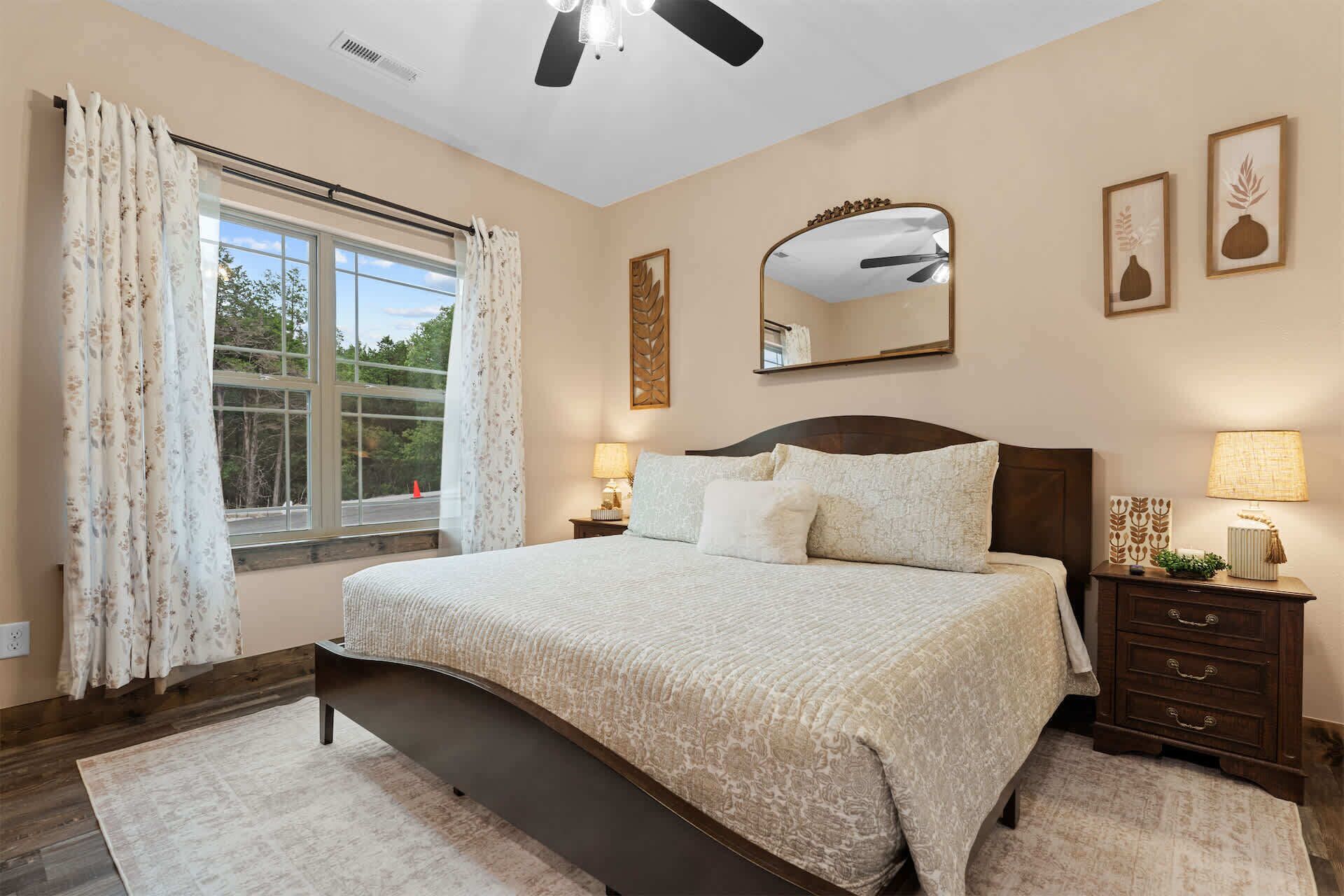 A bedroom with a large bed, a nightstand, a dresser, a window with curtains, and a ceiling fan.