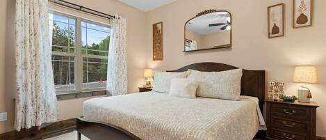 A bedroom with a large bed, a nightstand, a dresser, a window with curtains, and a ceiling fan.
