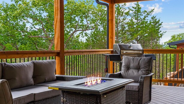 An outdoor deck with a grill, a cushioned seating area, and a fire feature. - The Lazy Beaver Lodge - Hot Tub (Hollister)