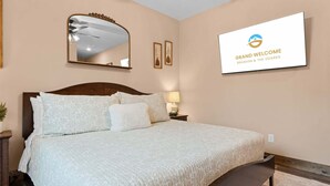 A bedroom with a large bed, a ceiling fan, a wall-mounted mirror, and a framed welcome sign. - The Lazy Beaver Lodge - Hot Tub (Hollister)