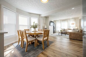 Ein geräumiger Wohnbereich mit Esstisch aus Holz, Stühlen, einer Couch und einem Fernseher.