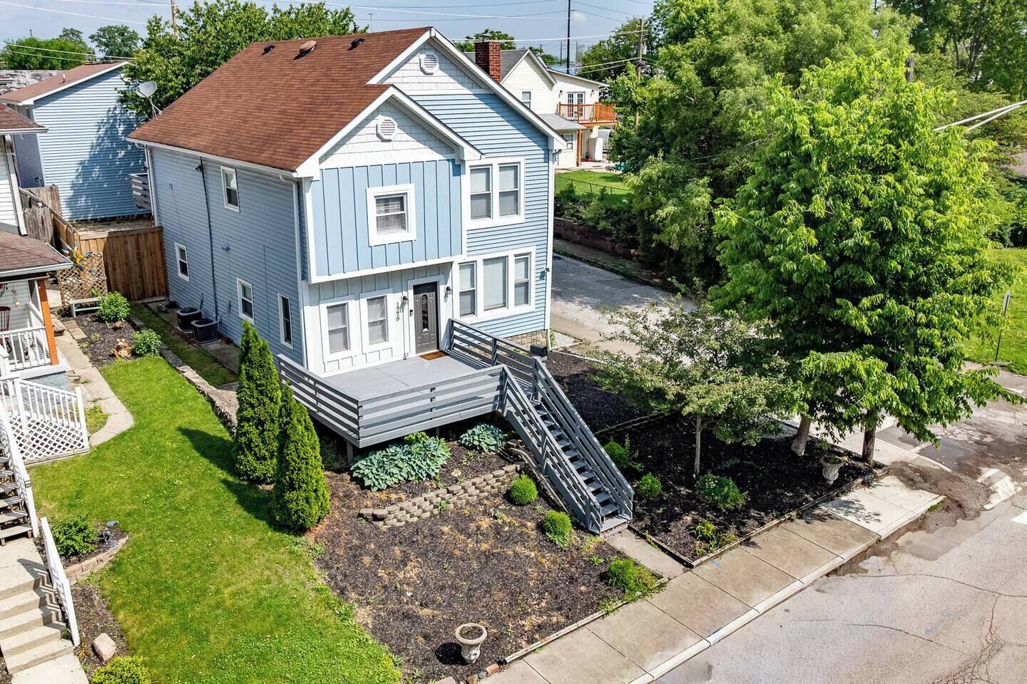 A two-story house with a front porch, a small front yard with a garden, and a staircase leading to the entrance.