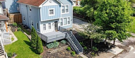 A two-story house with a front porch, a small front yard with a garden, and a staircase leading to the entrance.
