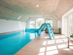 An indoor swimming pool with a blue slide, a sunlit room with large windows, and a bench. - 4 Star Holiday Home in Ulfborg (Ulfborg)
