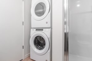 Ein kompaktes, weißes Wasch- und Trockner-Gerät an der Wand in einem Badezimmer mit einer Duschkabine aus Glas.