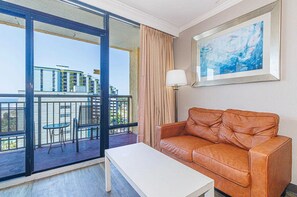 Ein Hotelzimmer mit Balkon, einer braunen Ledersofa, einem weißen Couchtisch und einem gerahmten abstrakten Gemälde.
