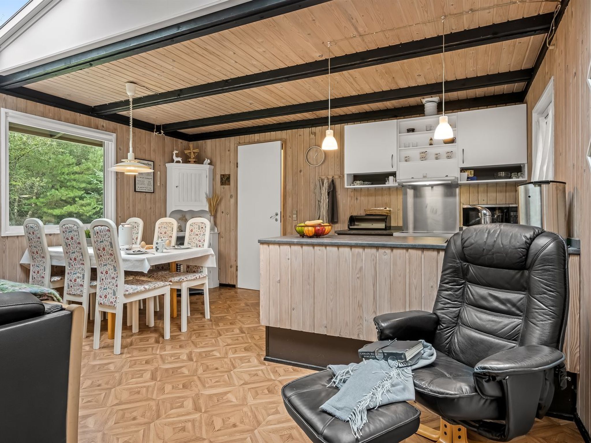 A modern kitchen with wooden cabinets, a dining area with floral chairs, and a black leather sofa.