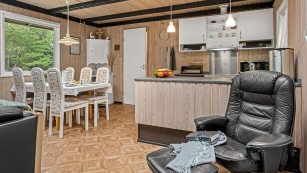 Eine moderne Küche mit Holzschränken, ein Essbereich mit floralen Stühlen und ein schwarzes Ledersofa.