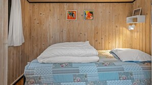 Ein Schlafzimmer mit Holzbalkendecke, zwei Gemälden, einem weißen Bett mit floralem Bettzeug und einem weißen Regal mit einem Bilderrahmen.