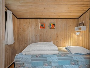 A bedroom with a wooden ceiling, two paintings, a white bed with floral bedding, and a white shelf with a picture frame. - "Hardina" - 1km from the sea by Interhome (Vejers Strand)