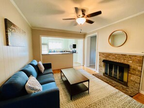 A living room with a sofa, coffee table, fireplace, and a ceiling fan. - Peaceful 4-bedroom ranch in Richmond’s west end. (Richmond)