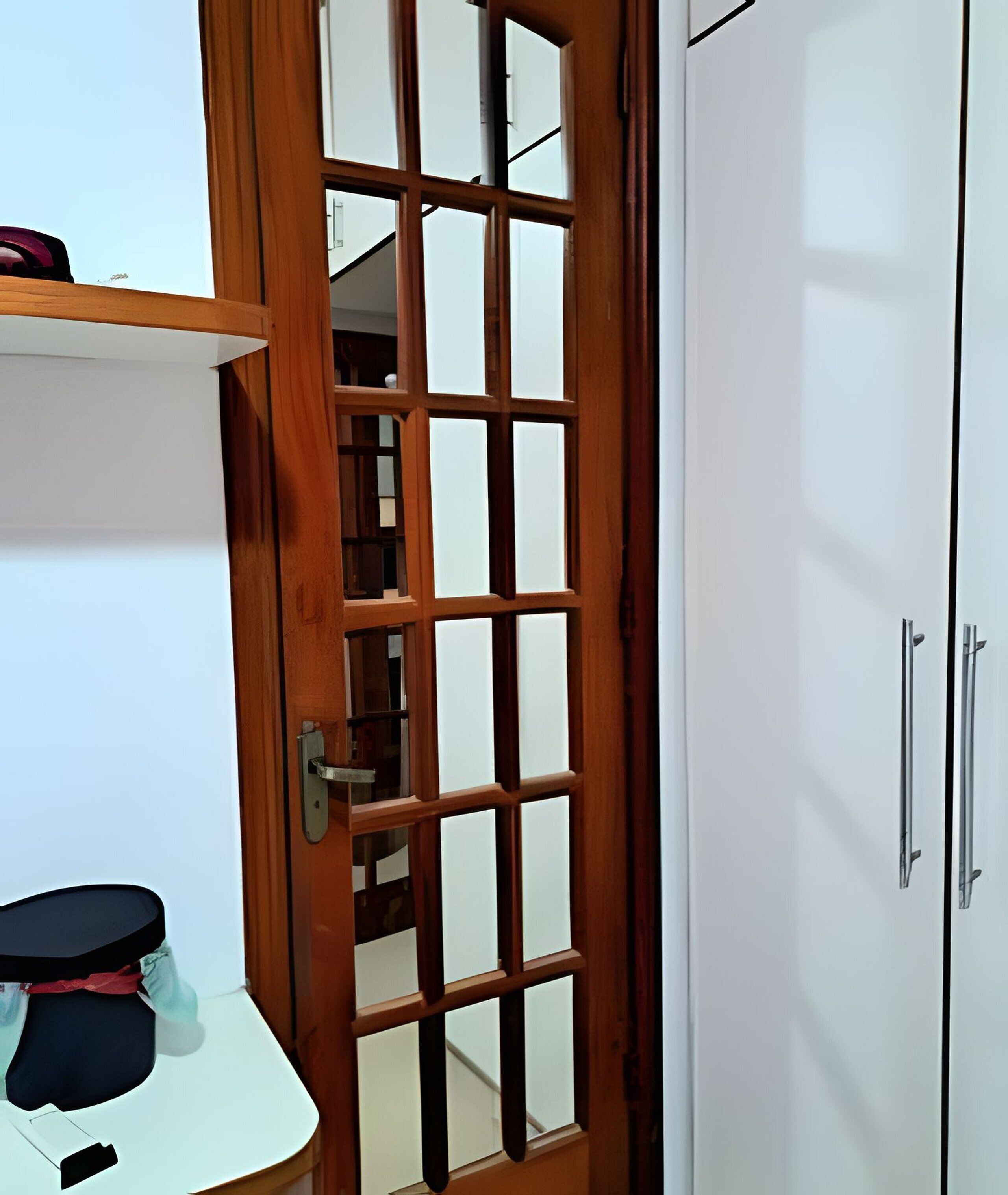 Una habitación con puerta de madera con paneles de vidrio, un armario blanco y un escritorio blanco con un objeto negro encima.