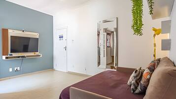 Una habitación moderna con televisión de pantalla plana, una cama con manta morada, un espejo y una planta colgante.
