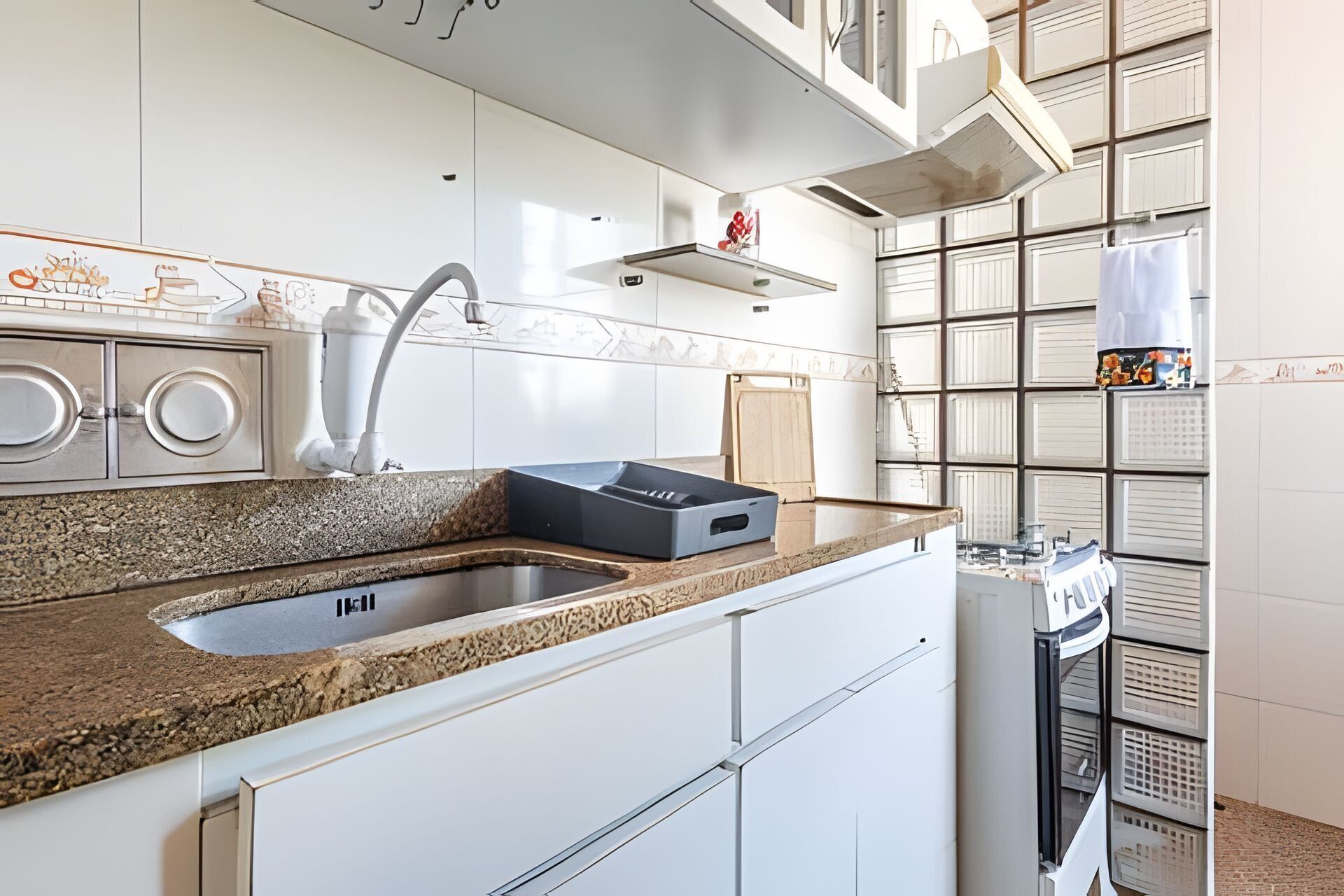 A modern kitchen with a granite countertop, stainless steel sink, and white cabinetry.