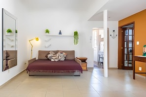 A modern bedroom with a bed, a bedside lamp, a small shelf with plants, and a view into the adjacent dining area. - Perto da Praia - Botafogo - HOTSPOT (Rio de Janeiro)