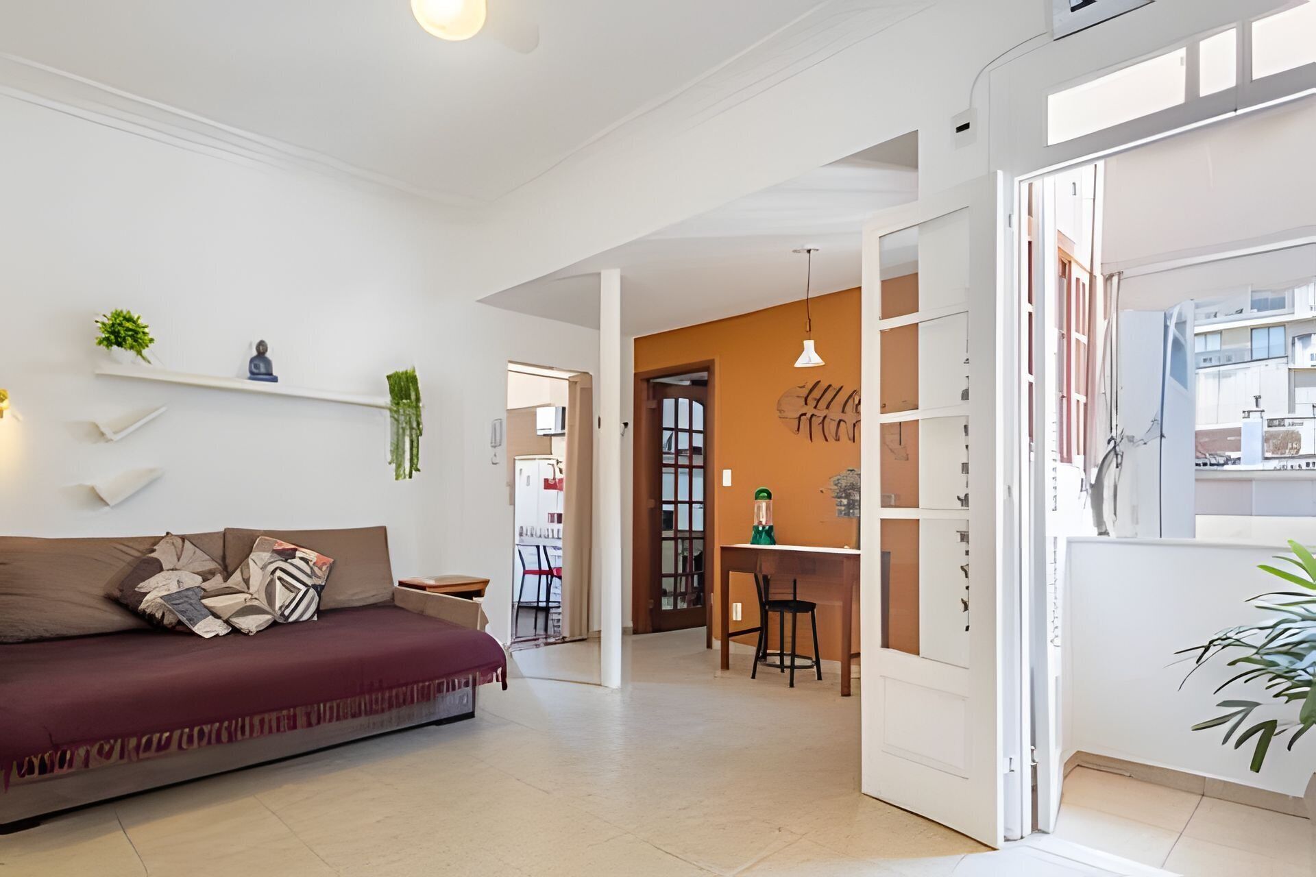 A modern living room with a sofa, a dining area, and a kitchen visible through an open door.
