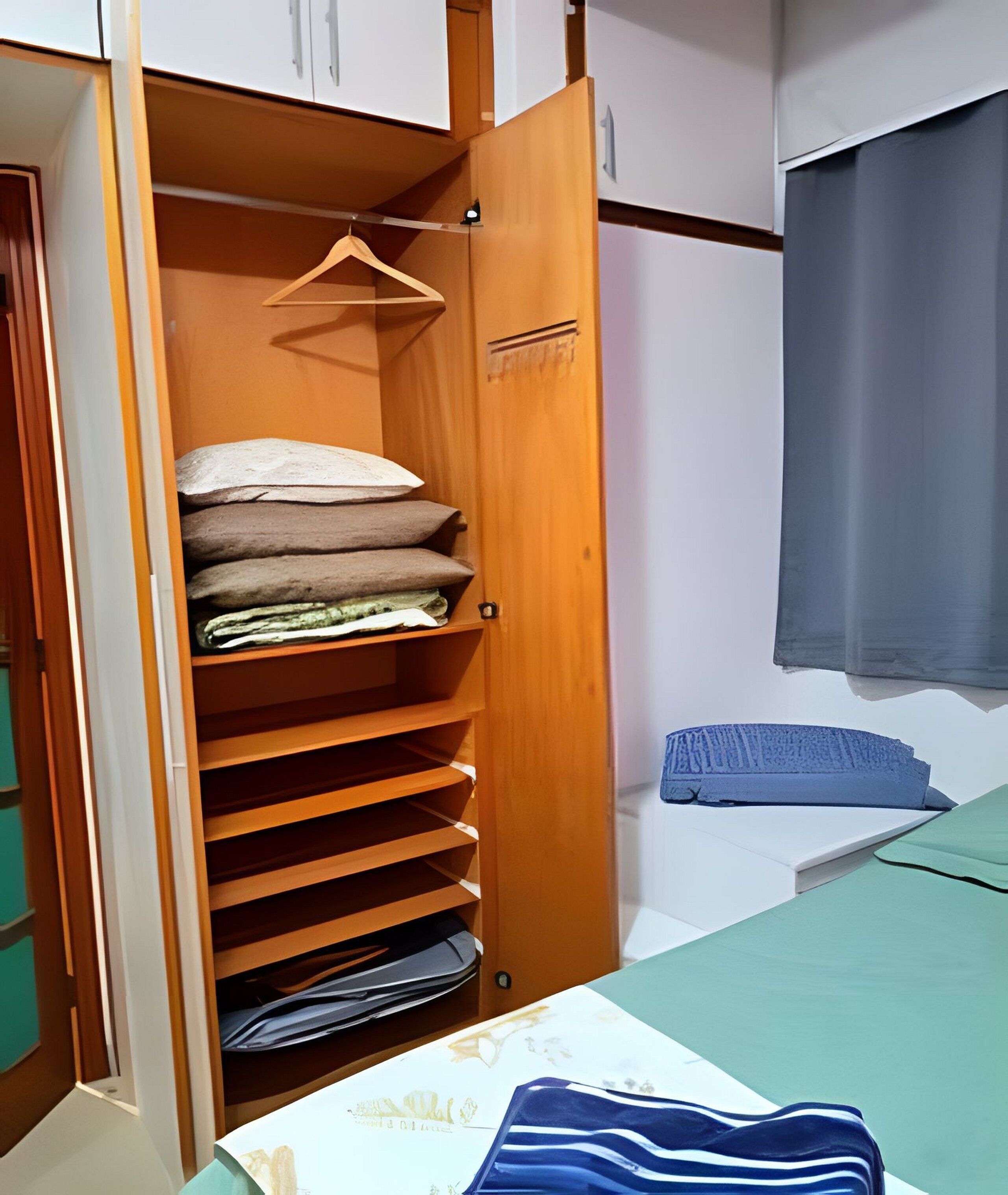 A bedroom with a bed, a wooden wardrobe with multiple shelves, and a small table with a blue and white striped cloth.